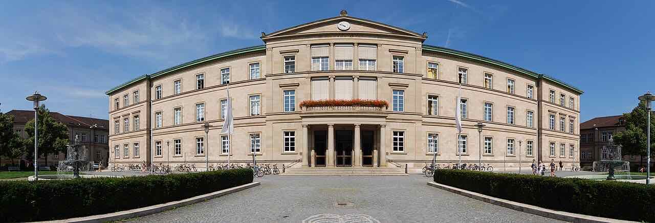 The wide classical front of the Neue Aula of the University of Tübingen on Wilhelmstraße, with a pillared entrance, fountains and parked bicycles