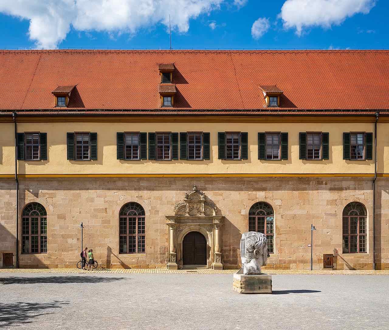 The north wing of Schloss Hohentübingen with a red tiled roof and a stone portal, and a large stone head sculpture in the courtyard