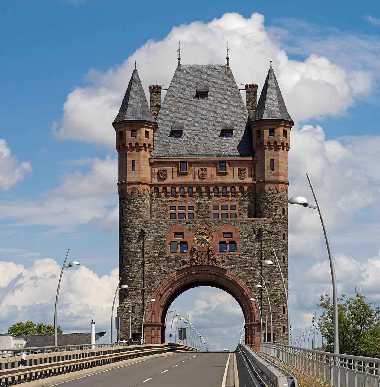 The red sandstone and dark stone bridge tower of the Nibelungen Bridge in Worms, seen straight on from the road with a big arch and two slate-roofed corner turrets