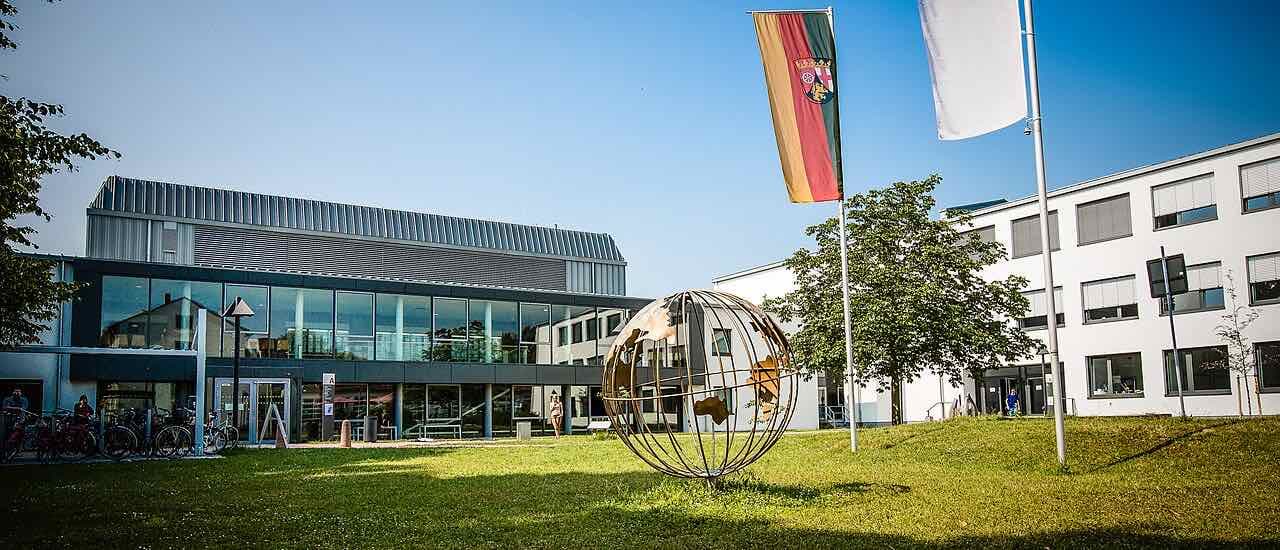 The Hochschule Worms campus on a sunny day: a glass-fronted building, a white building, a metal globe sculpture on the lawn and bicycles at the left