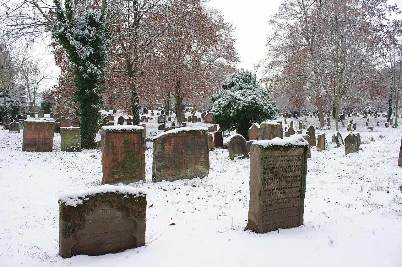 Old weathered gravestones with Hebrew inscriptions under bare trees and light snow in the Jewish cemetery Heiliger Sand